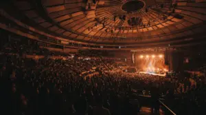 Interior del domo del Palacio de los Deportes durante un concierto, con el escenario iluminado en tonos cálidos y las gradas llenas