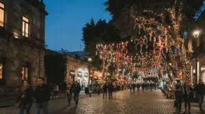 Calle peatonal de la Ciudad de México al anochecer, decorada con piñatas de estrella y luces navideñas entre los árboles